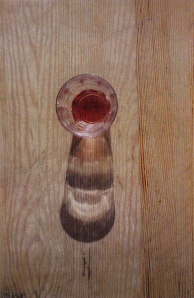 Een bijna leeg Frans wijnglas op een houten tafel recht van boven bekeken. De schaduw zorgt voor een abstract beeld.