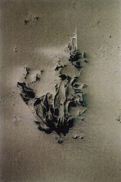 Een reliëf van iets, misschien is het een zwarte plastic zak, of een stuk stof, half bedekt door stuifzand.